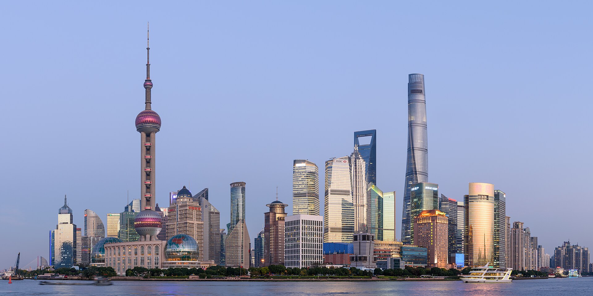 The Pudong skyline across the Huangpu River at dusk, with the Oriental Pearl Tower and Shanghai Tower